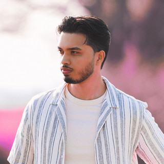 Zyrius wearing a white shirt against a softly blurred pink and gray background