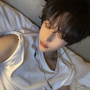 WONBIN resting against a pillow with earphones